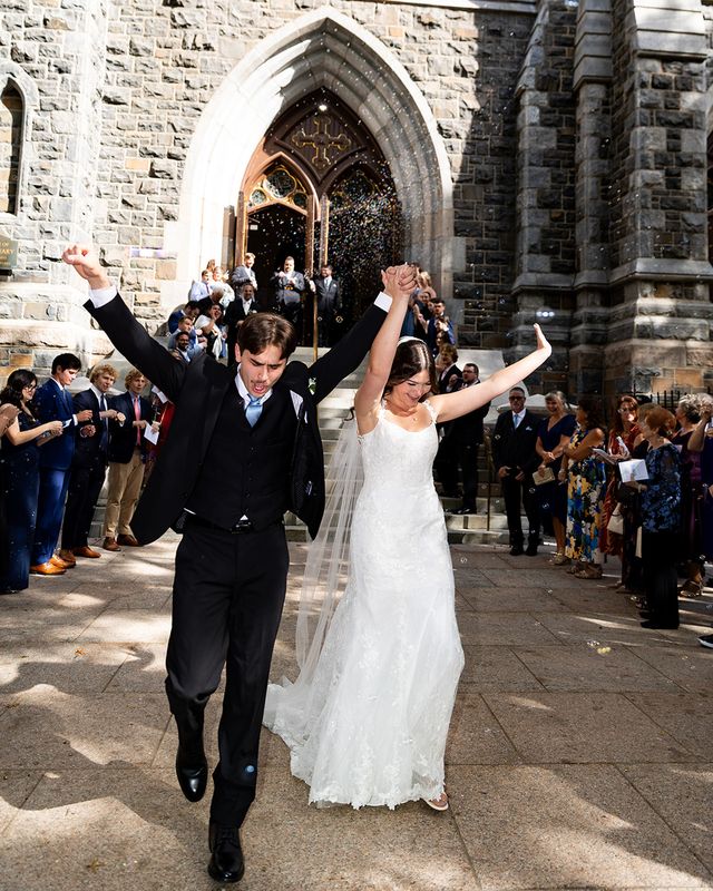 Joe and Hailey walking out of the church on their wedding day, arms raised, through a cloud of bubbles